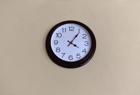 A black round clock with a white dial on a light wall. Stock Photos