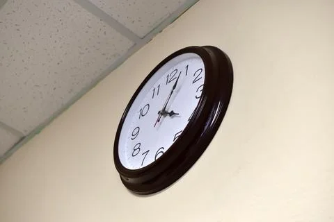 A black round clock with a white dial on a light wall. Stock Photos