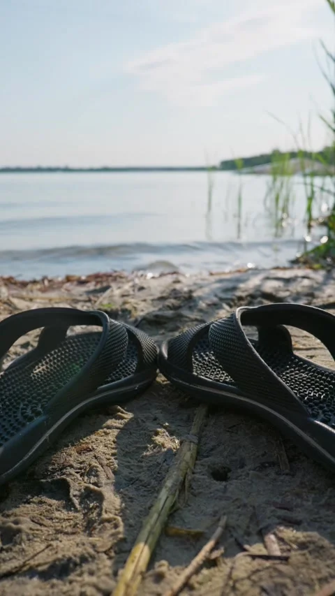 Black Rubber Flip Flop Sandals Resting on a Sandy River Beach Stock Footage 342184919