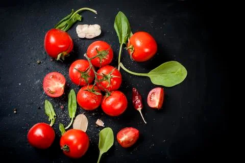 Black rustic tabletop with branch of tomatoes and herbs, top view Stock Photos