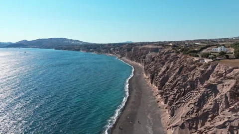 Black Sand Beach Under Eroded Brown Sea Wall near Santorini, Greece Aerial Track Stock Footage 344596097