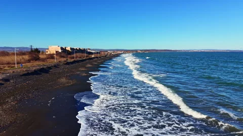 Black sand beach with waves and distant buildings near the shore during daylight Stock Footage 331159594