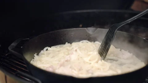 Black saucepan on bbq grid on burning charcoals, person stirring cut onion with Stock Footage 164396640