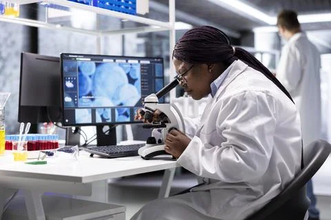 Black scientist examining samples under microscope in a modern laboratory Stock Photos