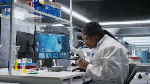 Black scientist examining samples under microscope in a modern laboratory 스톡 사진