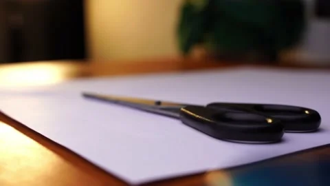Black scissors are placed on a white paper on a wooden table and taken Stock Footage 236678288