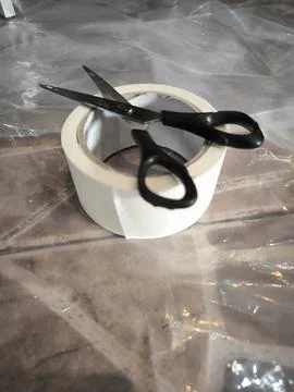 Black scissors lying on roll of white masking tape. Stock Photos