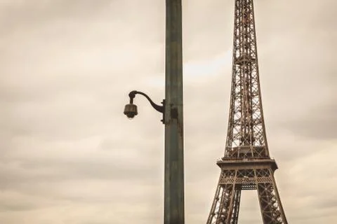 Black security camera on a pillar in bad weather in front of the Eiffel Tower Foto stock