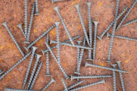 Black self-tapping screws scattered on a rusty sheet of metal, close-up, sele Foto stock