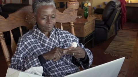 Black senior woman holding a pill bottle, video chatting on a laptop computer Stock Footage