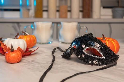 Black sequin mask with mini pumpkins and milk on marble surface Stock Photos