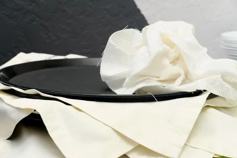 Black serving tray rests on a table covered with white linens and a crumpled Stock Photos