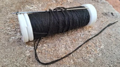Black sewing thread on a spool. Needle and dark yarn for tailoring and garment Stock Photos