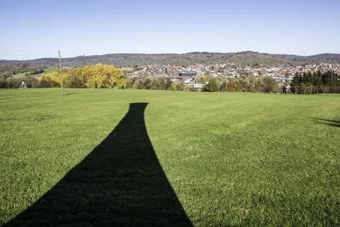 Black shadow of a tower on the green field near the town Stock Photos
