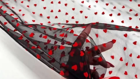 Black sheer mesh fabric features a red velvet heart pattern Video stock 333777857