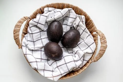 Black shiny easter eggs on a white towel in a brown basket on white background Foto stock