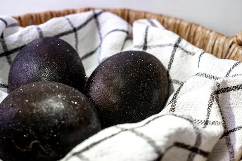 Black shiny easter eggs on a white towel in a brown basket on white background Foto stock