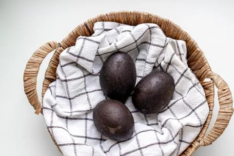 Black shiny easter eggs on a white towel in a brown basket on white background Stock Photos