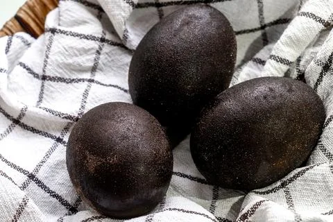Black shiny easter eggs on a white towel in a brown basket on white background Stock Photos