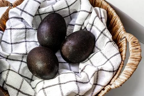 Black shiny easter eggs on a white towel in a brown basket on white background Stock Photos