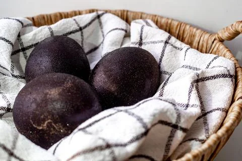 Black shiny easter eggs on a white towel in a brown basket on white background Foto stock