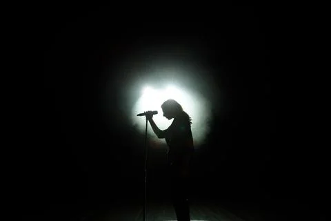 Black silhouette of female singer with white spotlights in the background Stock Photos