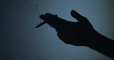 Black silhouette of a hand in which a cigarette on a blue background Stock Footage 123493210