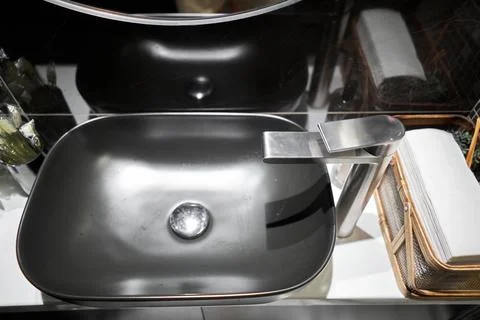 A black sink with a silver faucet next to an oval mirror and a shelf with hand Stock Photos