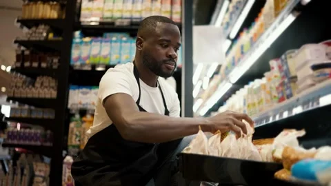 Of a Black-skinned man in a white t-shirt and black apron laying out bags of 動画素材 247050967