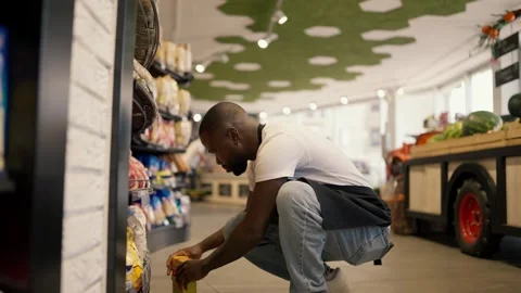 A Black-skinned man in a white t-shirt and black apron crouched near the display Видео 247051240