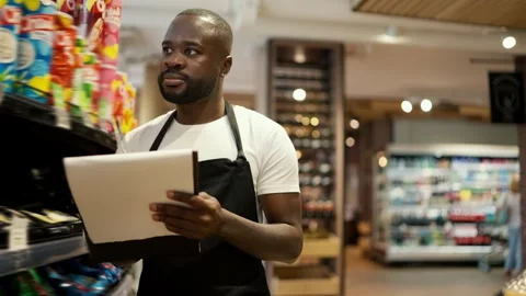 A Black-skinned man in a white t-shirt and a black apron walks along the windows Stock Footage 247051329