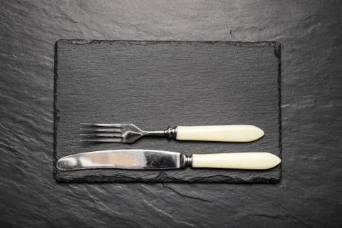 Black slate board for serving with fork and knife, top view Stock Photos