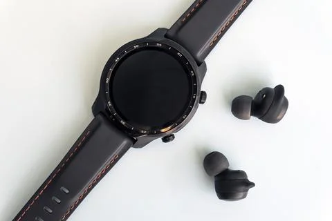 Black smart watch and wireless headphones on a white background. Blank screen Stock Photos
