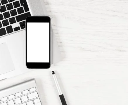 Black smartphone with blank screen lying over silver laptop on white table Stock-Fotos