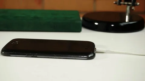 Black smartphone explodes while charging on white table. Slowmo Stock Footage 125432626