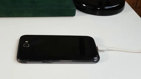 Black smartphone explodes while charging on white table. Video stock 125432651