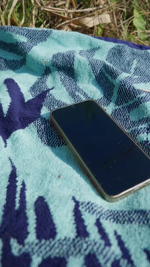 Black Smartphone Lying on a Blue Patterned Beach Towel Outdoors Stock Footage 342769758