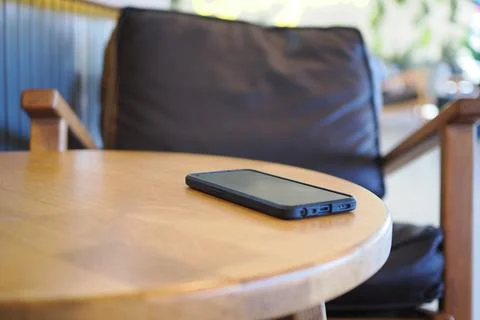 Black smartphone on wooden table in cafe setting. lost smart phone concept Stock Photos