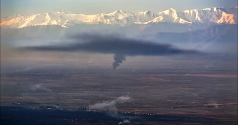 Black smoke spreads over rural valley before sunlit Caucasus mountains Stock Footage 344226505