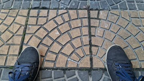 Black sneakers standing on patterned concrete paving stones outdoors Stock Photos