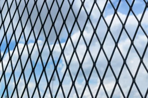 Black solid metallic mesh fence closeup with sky in the background. Stock Photos