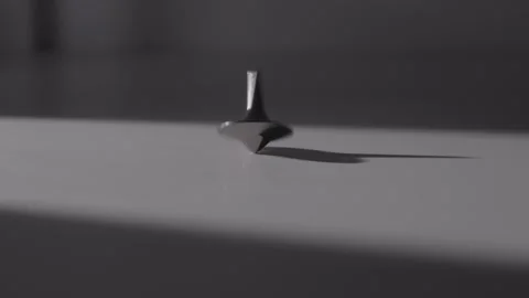 Black Spinning Top Rotating and Tipping Over on White Surface Stock Footage 336550149
