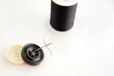 Black spool of thread, needle, and black and white buttons Stock Photos