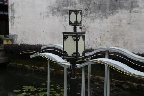 Black square lantern post beside wavy light forms over a shallow garden pond Stock Photos