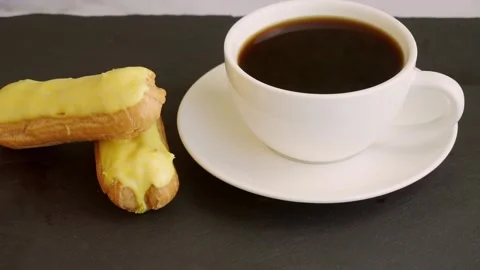 On a black stand is a white cup with black coffee and lemon eclairs. Stock Footage 204739723