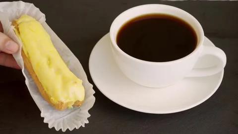 On a black stand is a white cup with black coffee and lemon eclairs. Stock Footage 204739959