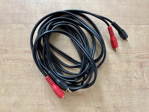 Black stereo cable with red and black connectors on wooden surface Stock Photos