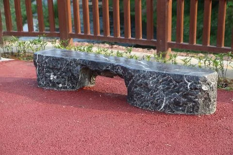 Black stone bench on red paved path beside wooden railing Stock Photos