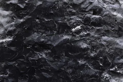 A black stone surface with an uneven texture in the form of bulges and cracks in Stock Photos