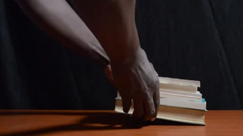 Black student places a stack of books on a table with black background Stock Footage 276593765